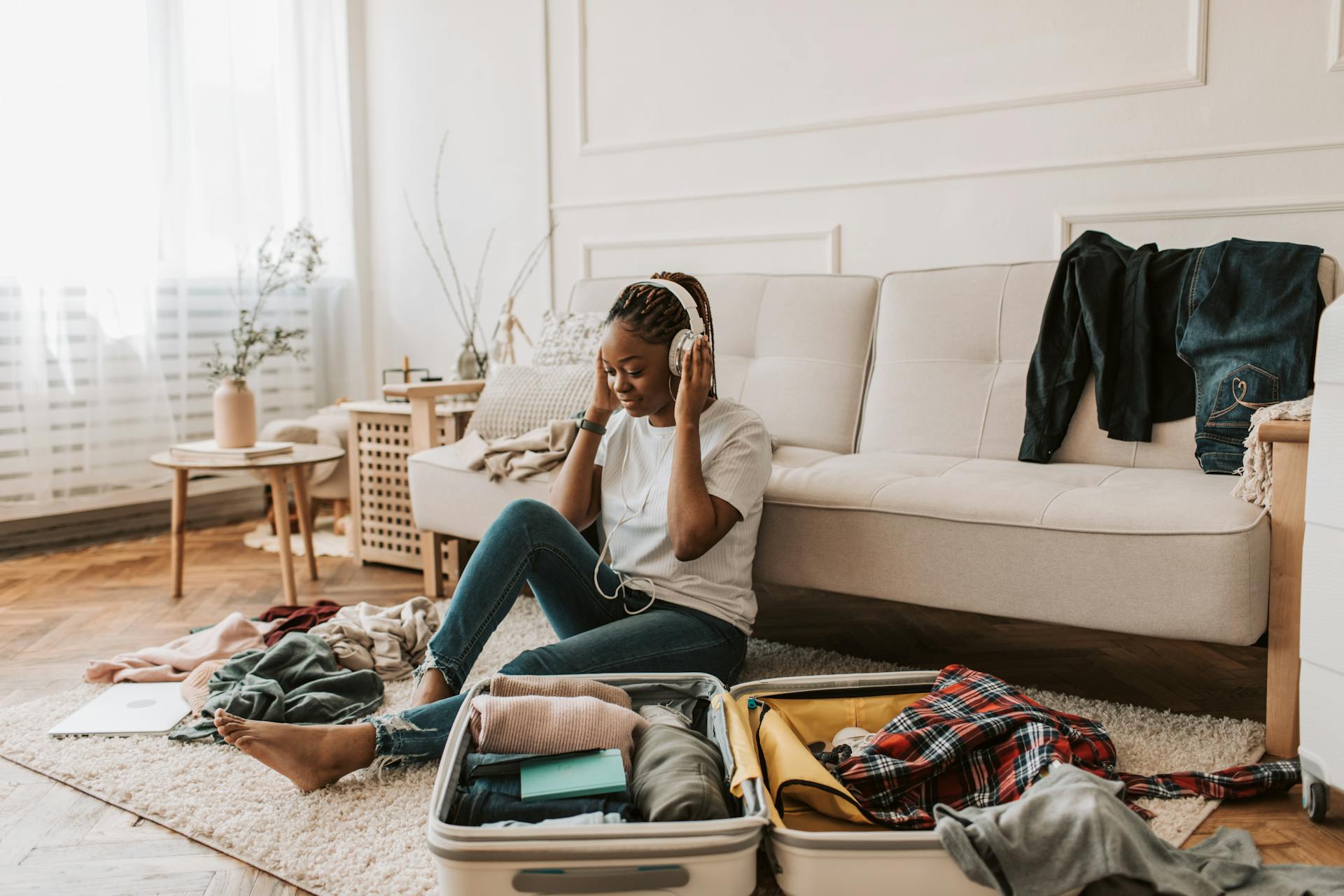 A young woman wearing headphones sits on the floor packing a suitcase, preparing for a trip.