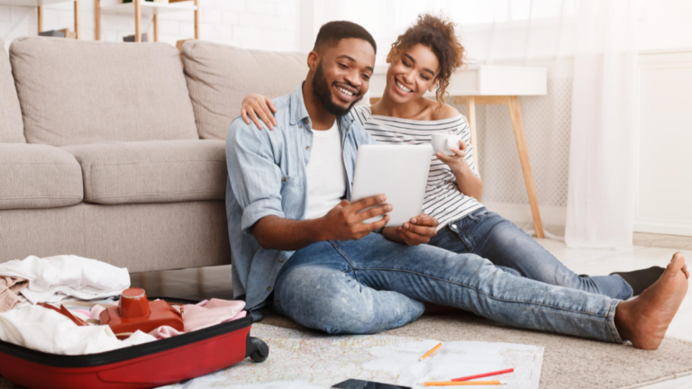 Young couple on living room floor comparing travel insurance options.