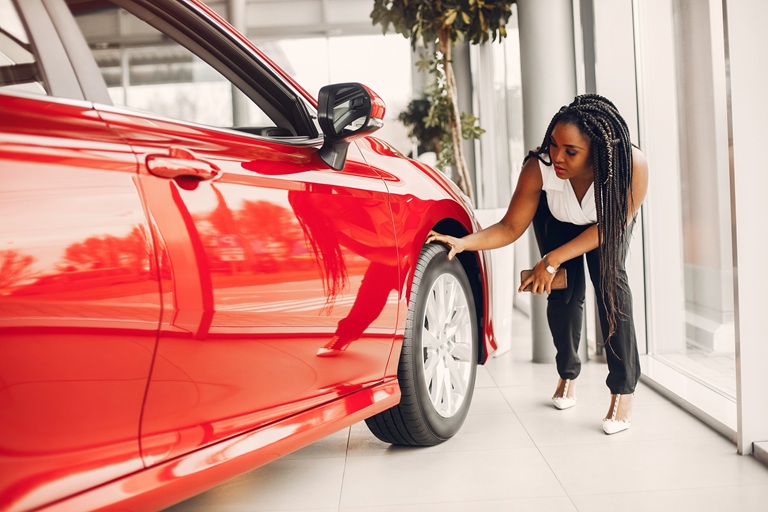 A woman scanning the tire of a rental car while considering car hire excess insurance