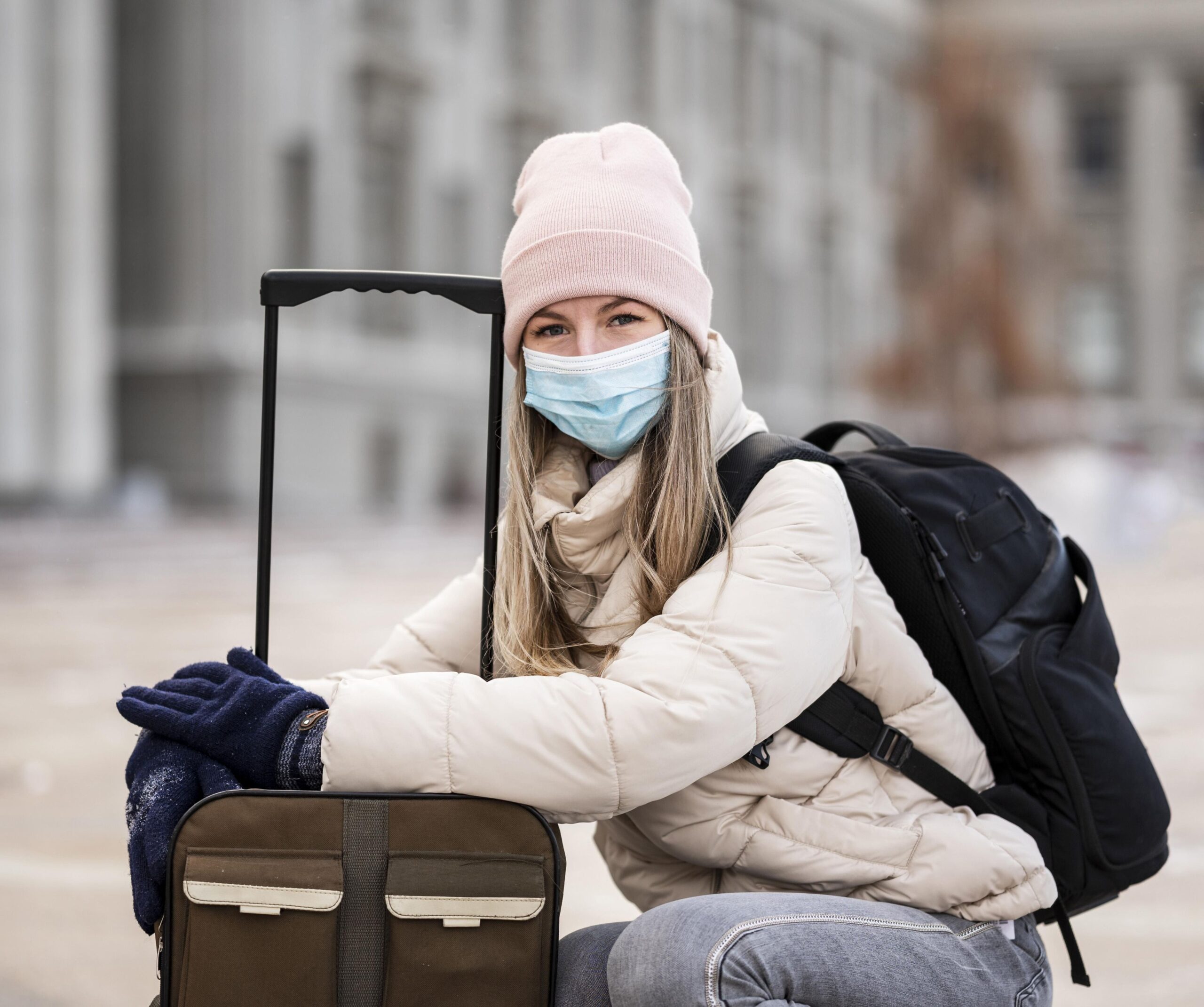 A woman travelling with luggage, wearing a mask to demonstrate travel insurance vs medical aid