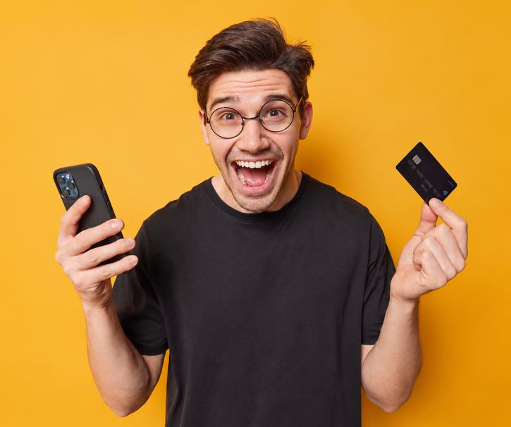 Man holding a smartphone and credit card against a yellow background.